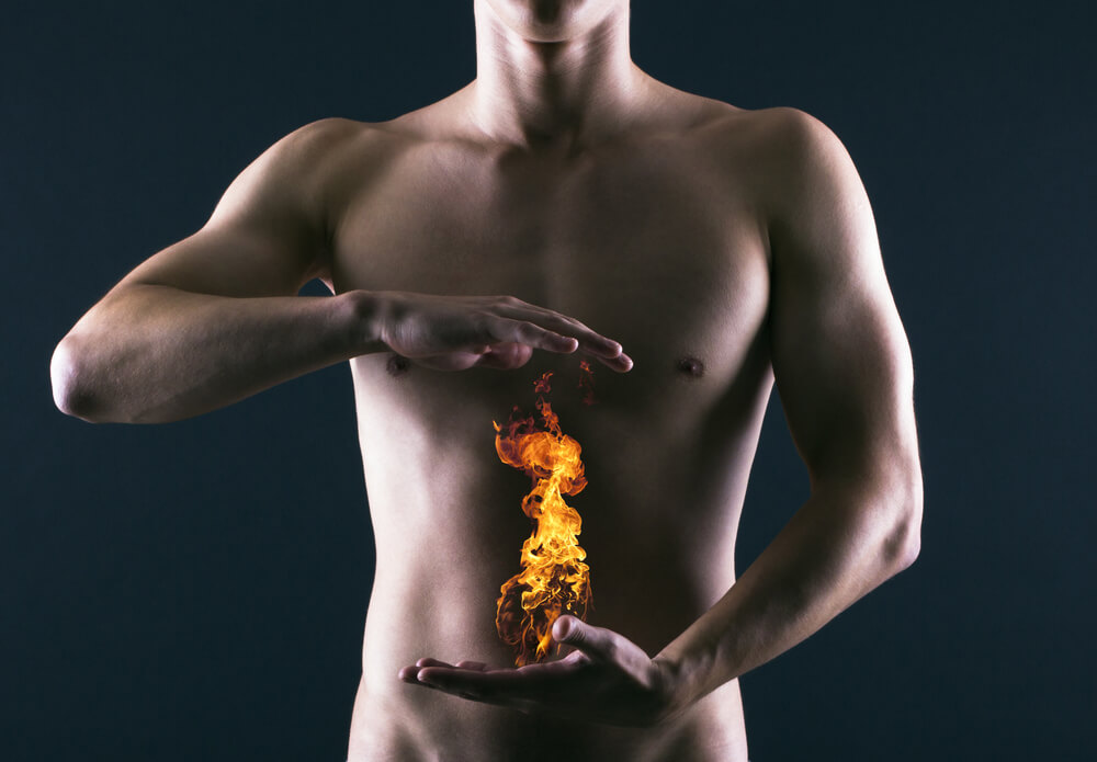Gol moški navidezno drži plamen ognja pred trebuhom kot pokazatelj, da ga muči zgaga.