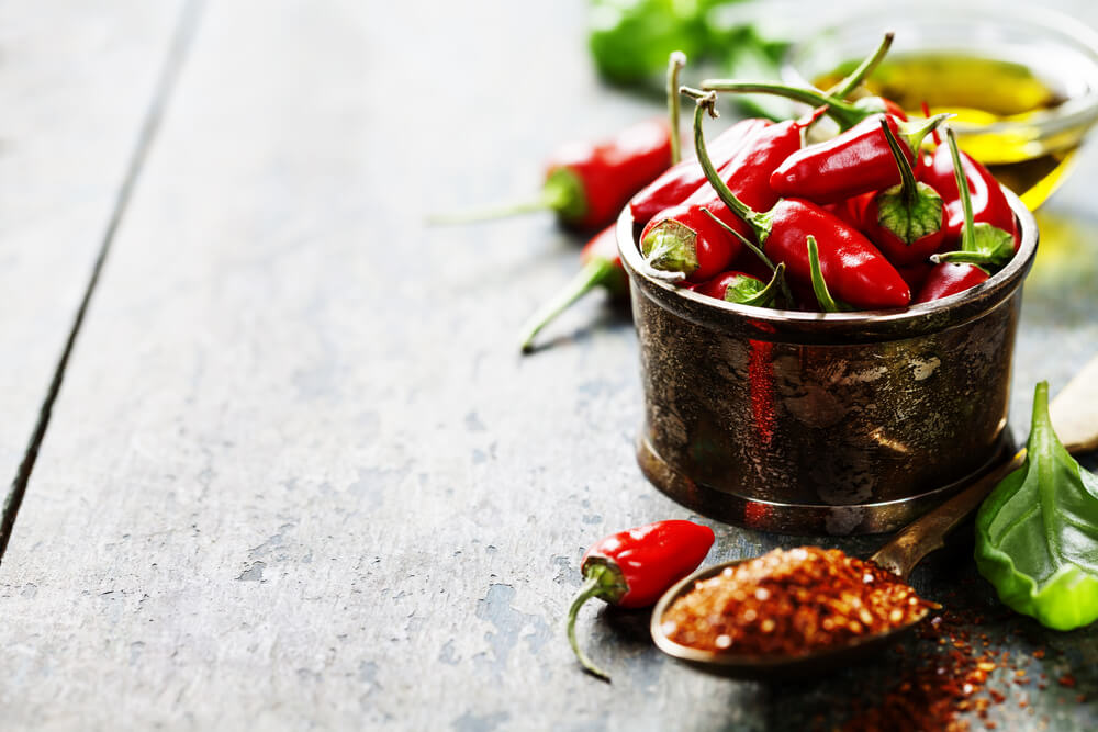 Frisch gepflückte rote Chilischoten in einer Metallschale, dazu gibt es Kräuter und Gewürze auf einem Löffel.