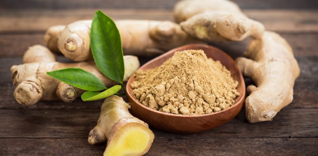 Ginger roots and ground ginger in a wooden bowl.