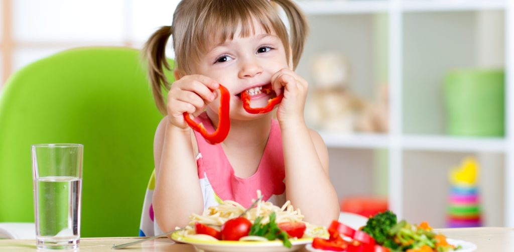 A little girl is eating a healthy meal at home with a smile on her face.