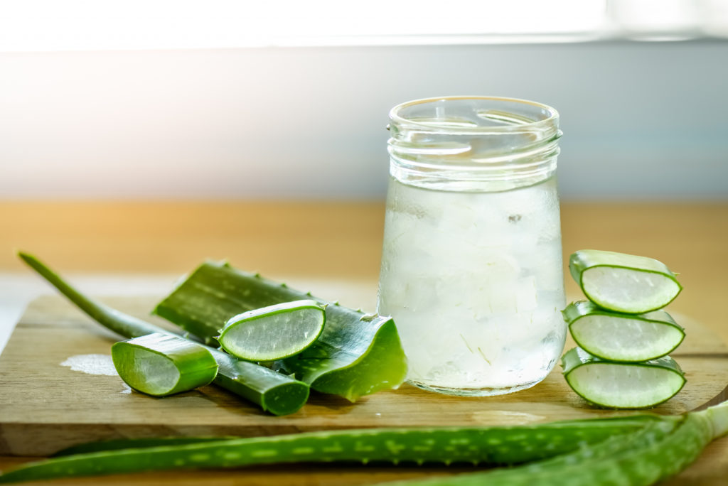 Una foglia fresca di aloe vera e un bicchiere di succo di aloe vera su un tagliere di legno.