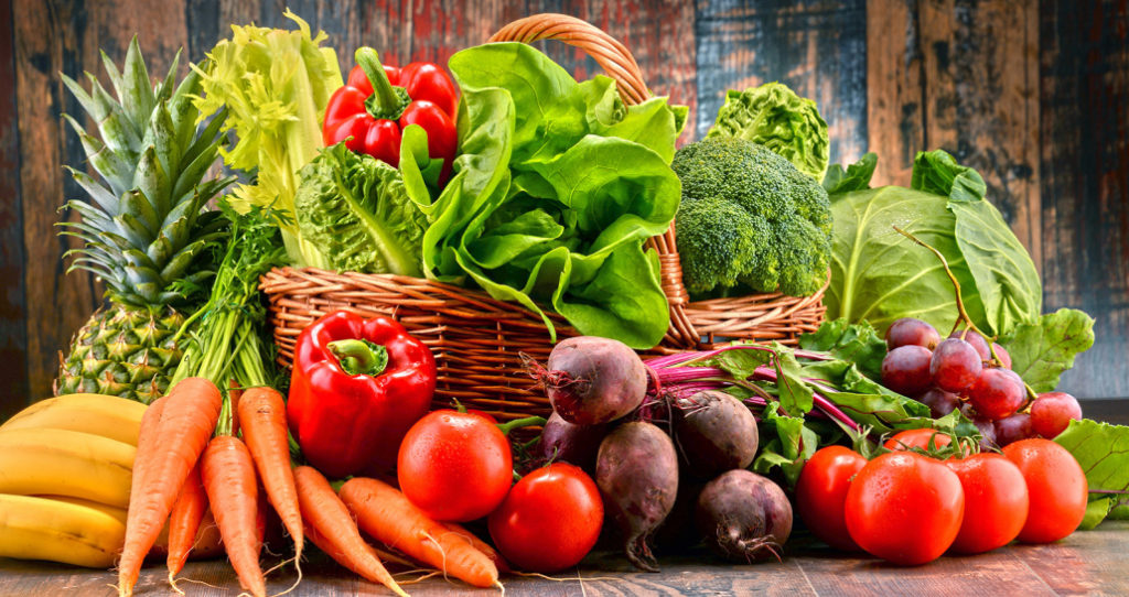 Raw organic vegetables inside and around a wicker basket.