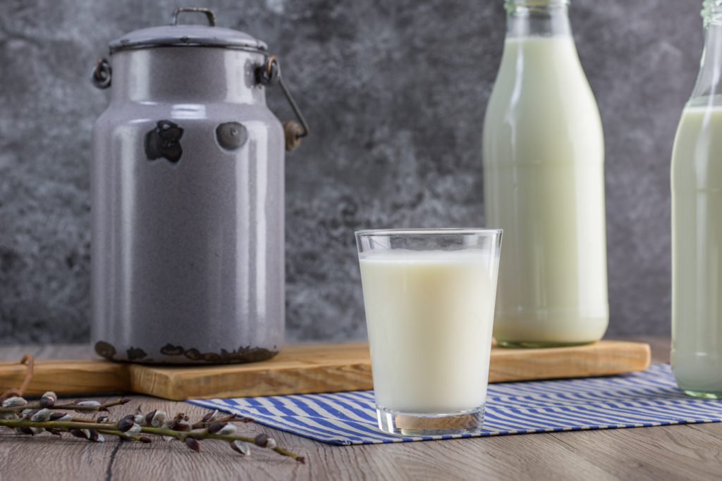 A pitcher of milk, a glass of milk and two bottles of milk on a wooden table.