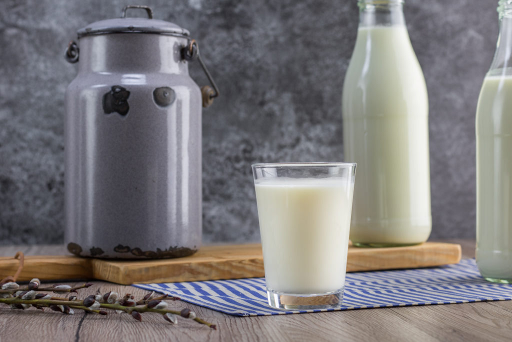 Ein Krug Milch, ein Glas Milch und zwei Flaschen Milch auf einem Holztisch.