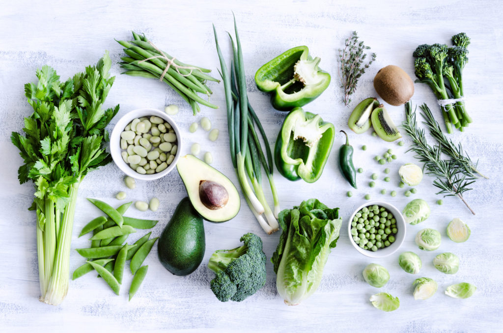 Grünes Gemüse, Obst und Gewürze auf grauem Hintergrund.