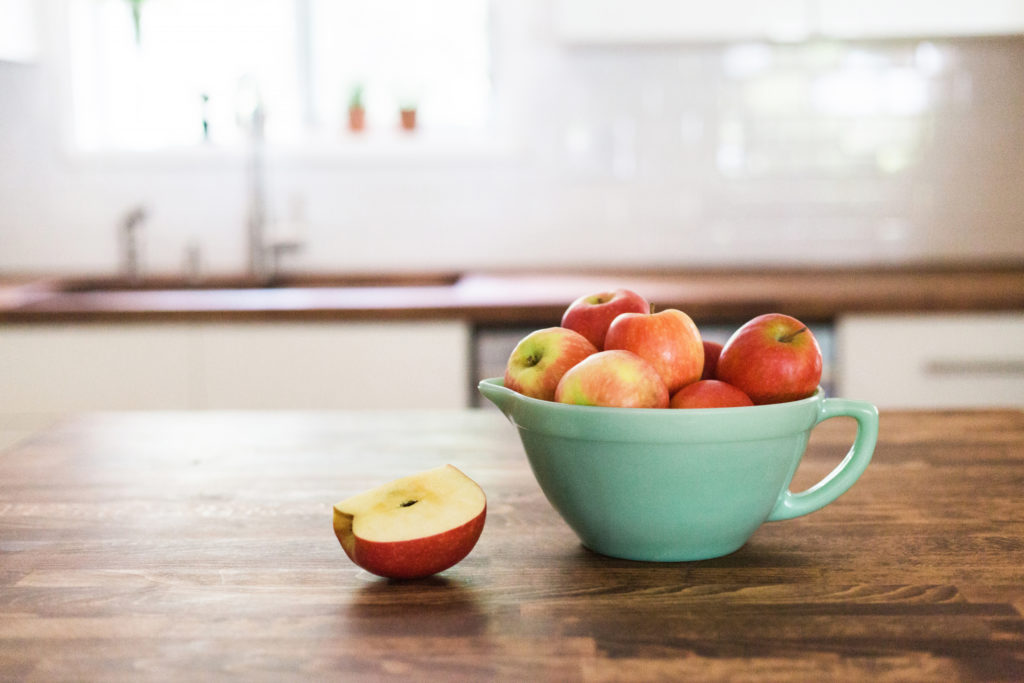Turquoise green bowl full of red apples on a modern wooden kitchen counter.