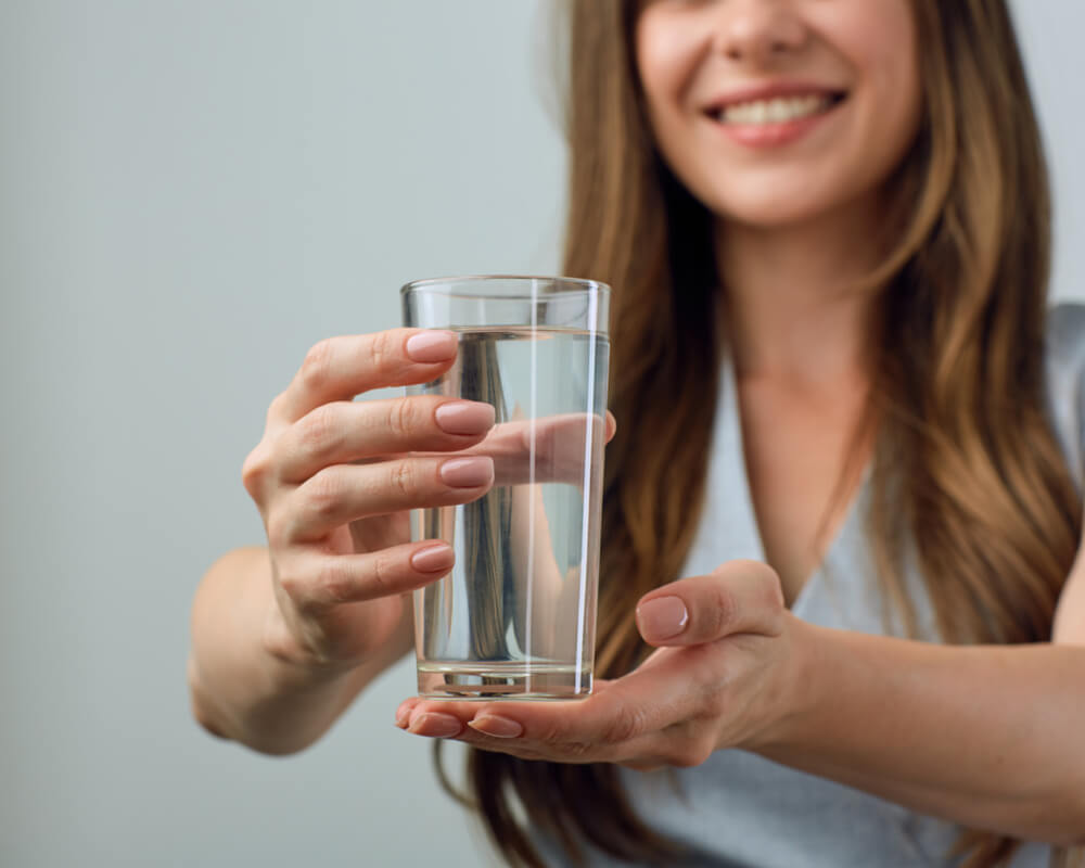 A healthy woman is holding a glass of mineral water.