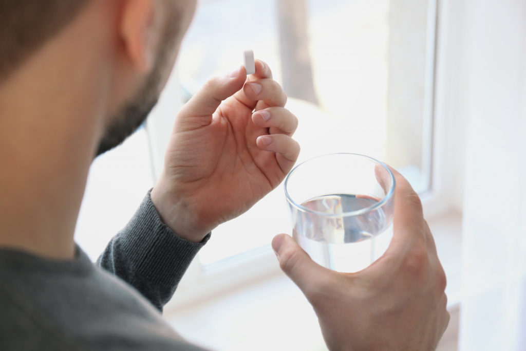 Ein Mann hält in der einen Hand ein Abführmittel und in der anderen ein Glas Wasser.