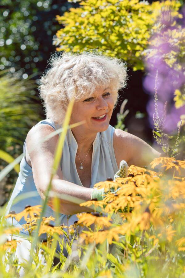 An elderly woman arranges flowers in her garden.