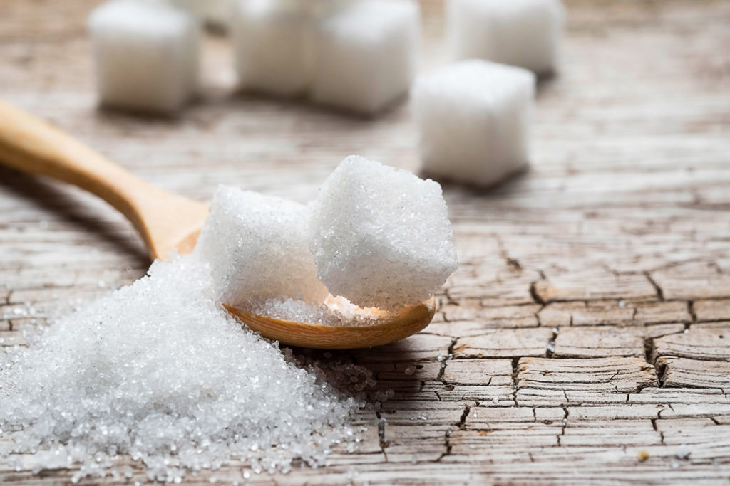 White sugar cubes on a wooden spoon that is set on a wooden table.
