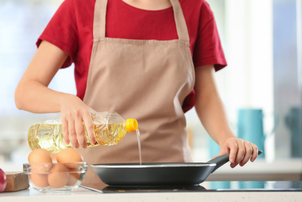 Una donna versa dell'olio alimentare da una bottiglia di plastica in una padella sui fornelli.