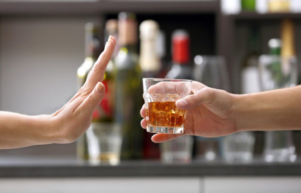 A woman is signaling with her hand that she does not want an alcoholic drink offered to her in a glass by a man.