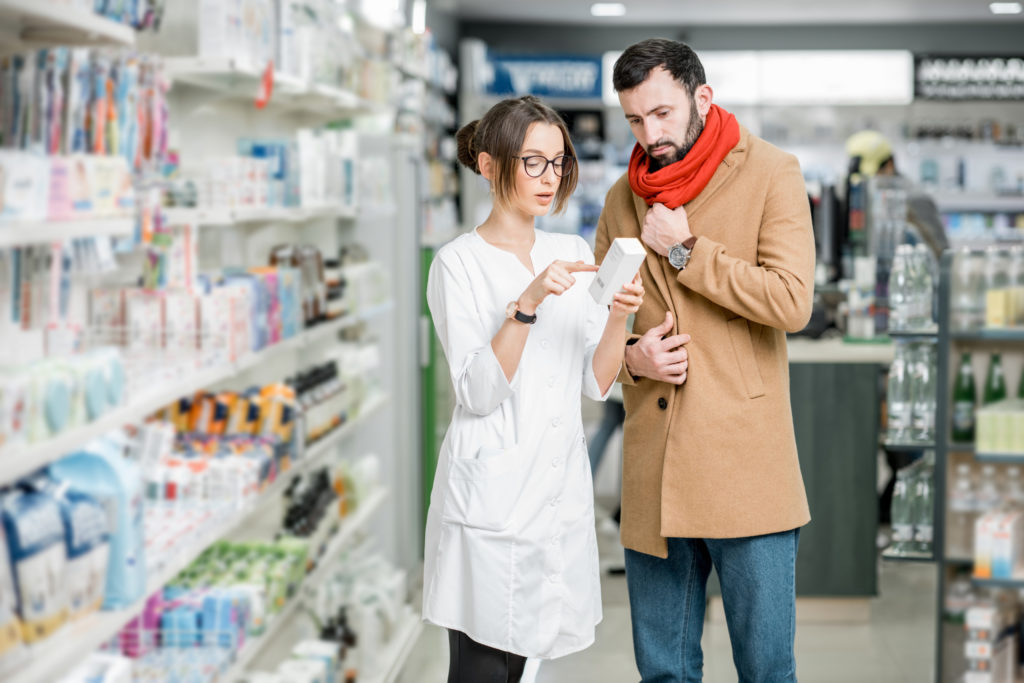 A helpful pharmacist is advising a sick man in a pharmacy.