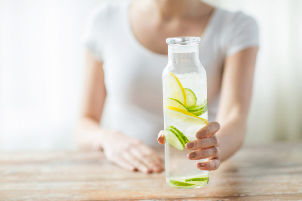 Eine Frau hält eine Flasche mit Wasser und geschnittenen Gurken- und Zitronenscheiben.