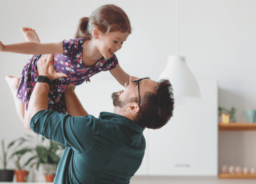 A happy dad is lifting his daughter high up in the air. They are both laughing hard.