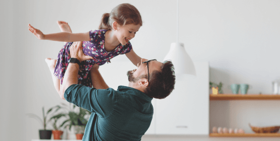 A happy dad is lifting his daughter high up in the air. They are both laughing hard.
