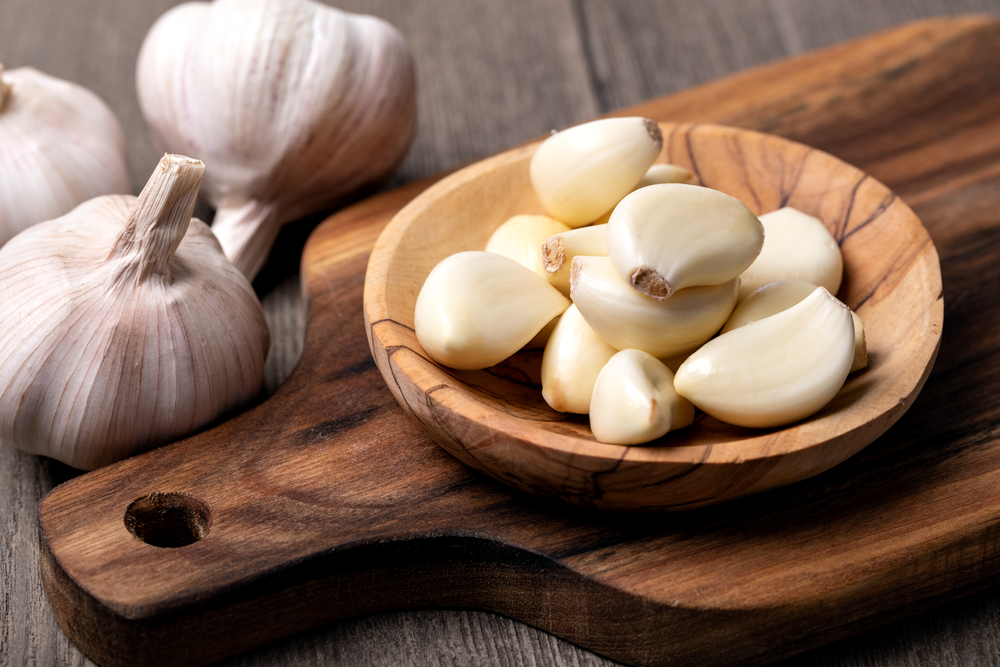 Spicchi d'aglio, sbucciati e con la buccia, su una tavola di legno.