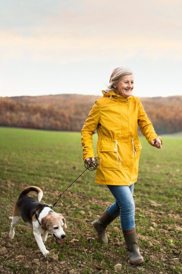 Nasmiješena gospođa u žutoj kabanici u šetnji sa psom.