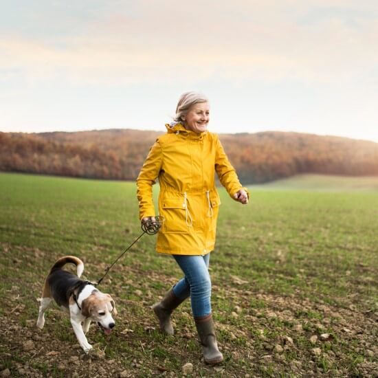Улыбающаяся женщина в желтом плаще гуляет с собакой.