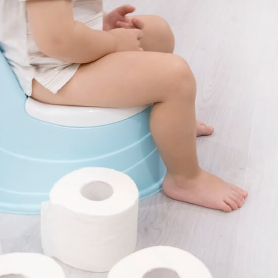 A little child is sitting on a blue potty and there is a toilet paper roll next to her.