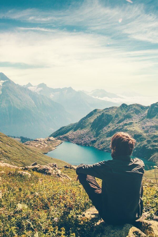 A traveler who is meditating by relaxing on a rock and admiring the magnificent view of the mountains and the lake.