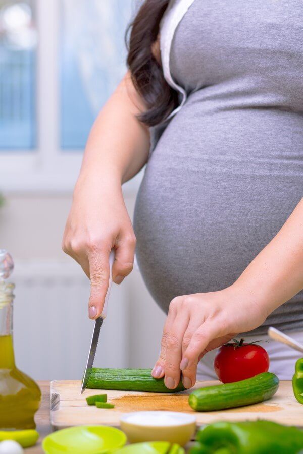 A pregnant woman is cutting vegetables for healthy lunch.