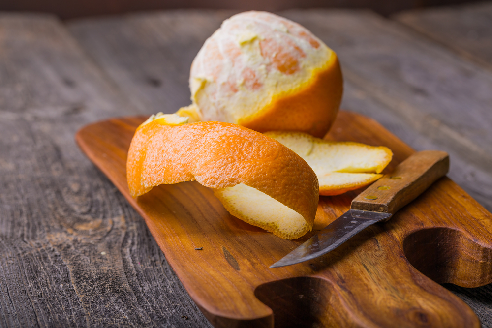Olupljena pomaranča na leseni deski za rezanje.