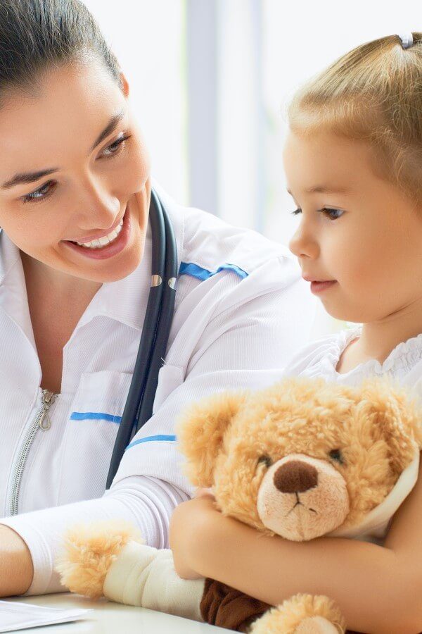 A little girl with a teddy is at the doctor’s.
