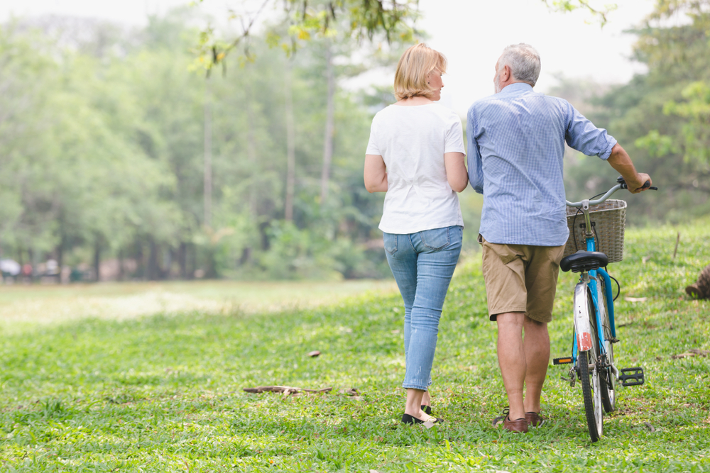Im Hintergrund sehen wir ein älteres Ehepaar, das neben dem Fahrrad durch den Park spaziert und sich fröhlich unterhält.