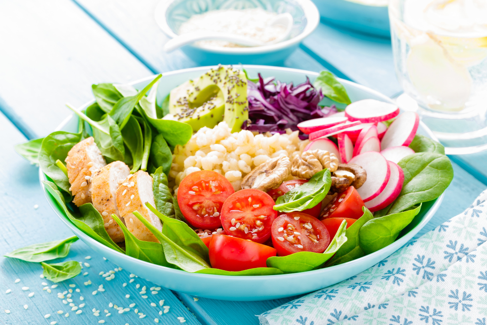 A rich salad plate with spinach, avocado, walnuts, radishes, cabbage and tomatoes.