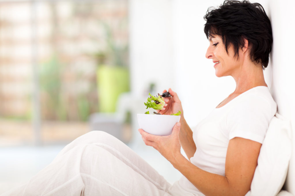 Una signora in forma, di una certa età, mangia un insalata perché ci tiene a una sana digestione.