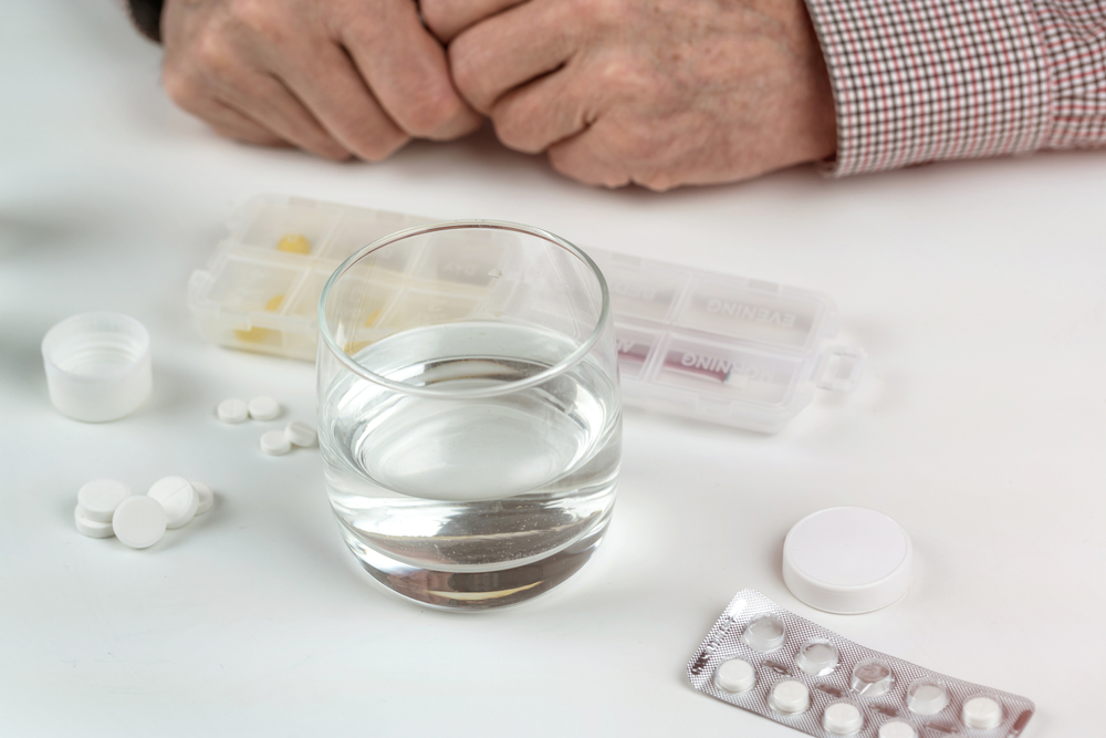 Много разных таблеток на белом столе и руки пожилого мужчины.