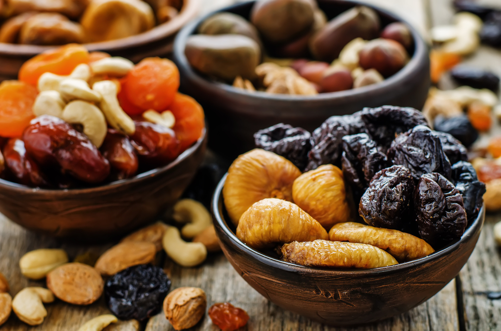 A mix of dried fruit and nuts in wooden bowls on a wooden table.