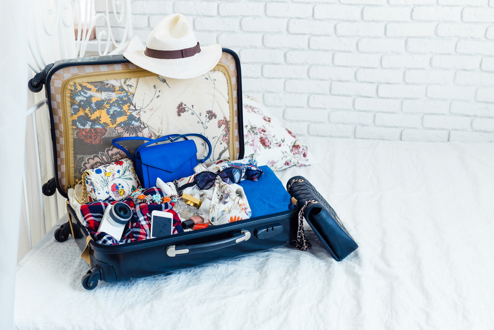 An open full suitcase on a white bed.