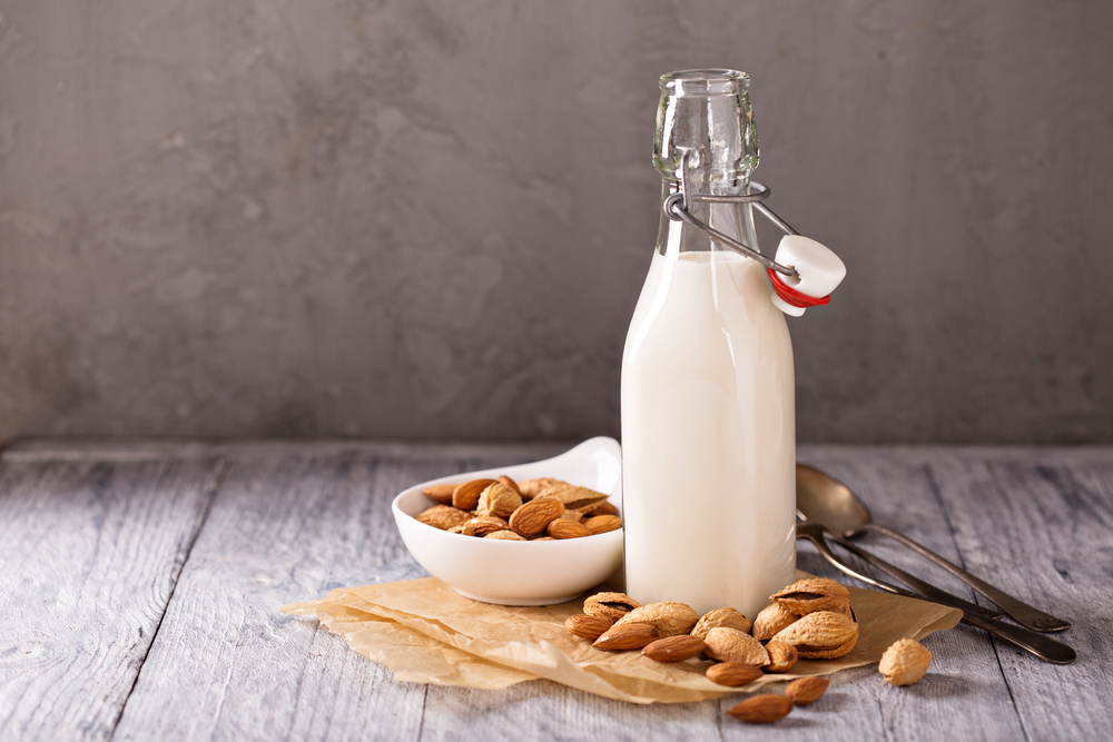 Homemade almond milk in a small glass bottle that is surrounded by almonds.