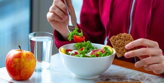 An employee is having lunch at his workplace – a salad and crackers.
