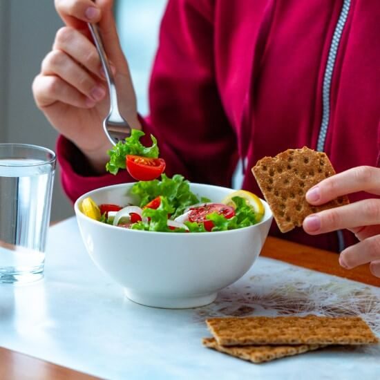 An employee is having lunch at his workplace – a salad and crackers.