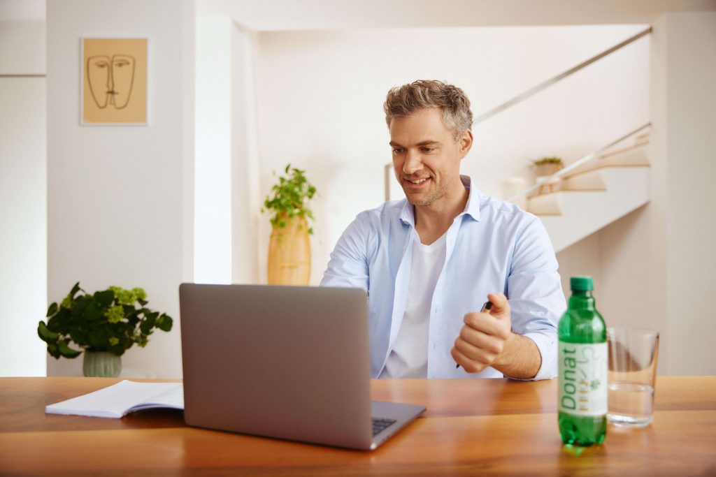 Un uomo lavora da casa al computer e beve Donat.