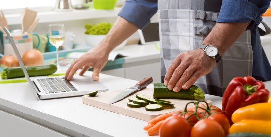Person preparing vegetables in the kitchen while using a laptop