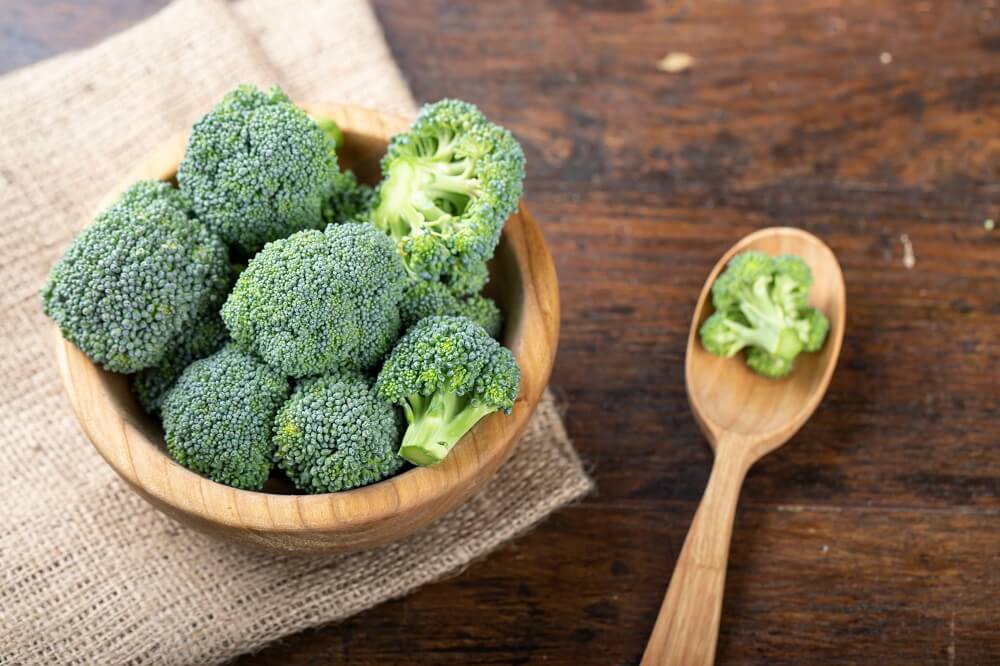 Broccoli in a wooden bowl and wooden spoon.