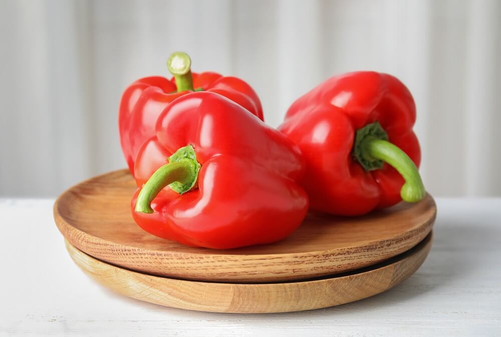 A red bell pepper on a wooden platter.