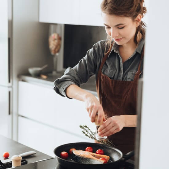 Mlada ženska peče lososa za kosilo, saj vsebuje veliko omega-3 maščobnih kislin.