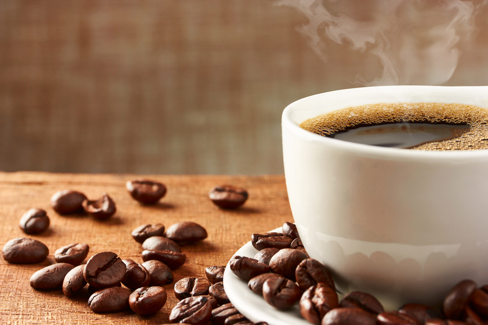 Una tazza di caffè caldo con accanto dei chicchi di caffè.