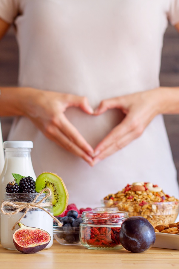 Žena oblikuje srce rukama ispred svog stomaka, jer uživa u ishrani koja je dobra za njezinu probavu – jogurt, voće, bobičasto voće, orašasti plodovi iz organske proizvodnje.