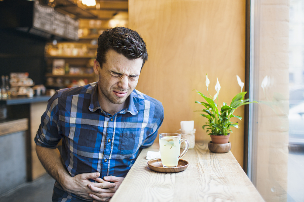 Un uomo è seduto al bar, beve un tè e si tiene la pancia perché ha problemi di digestione.