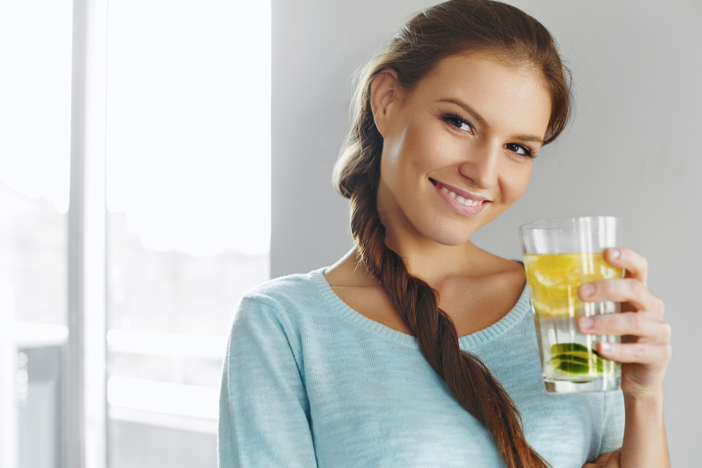 A happy woman holds in her hands a glass of water with lemon and mint.