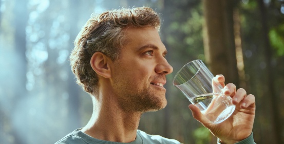 Мужчина пьет воду из стакана.