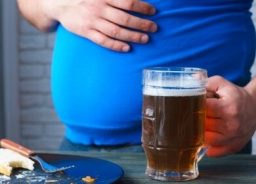 A man with a mug of beer in one hand, holding on to his stomach with the other.