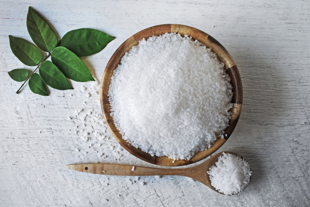 Salt in a wooden bowl, next to it is salt on a wooden spoon.