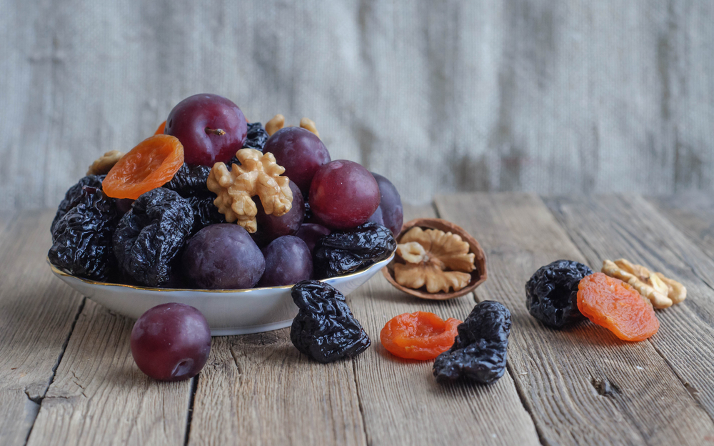 Fresh and dried prunes, walnuts and dried apricots in a bowl on a wooden counter.